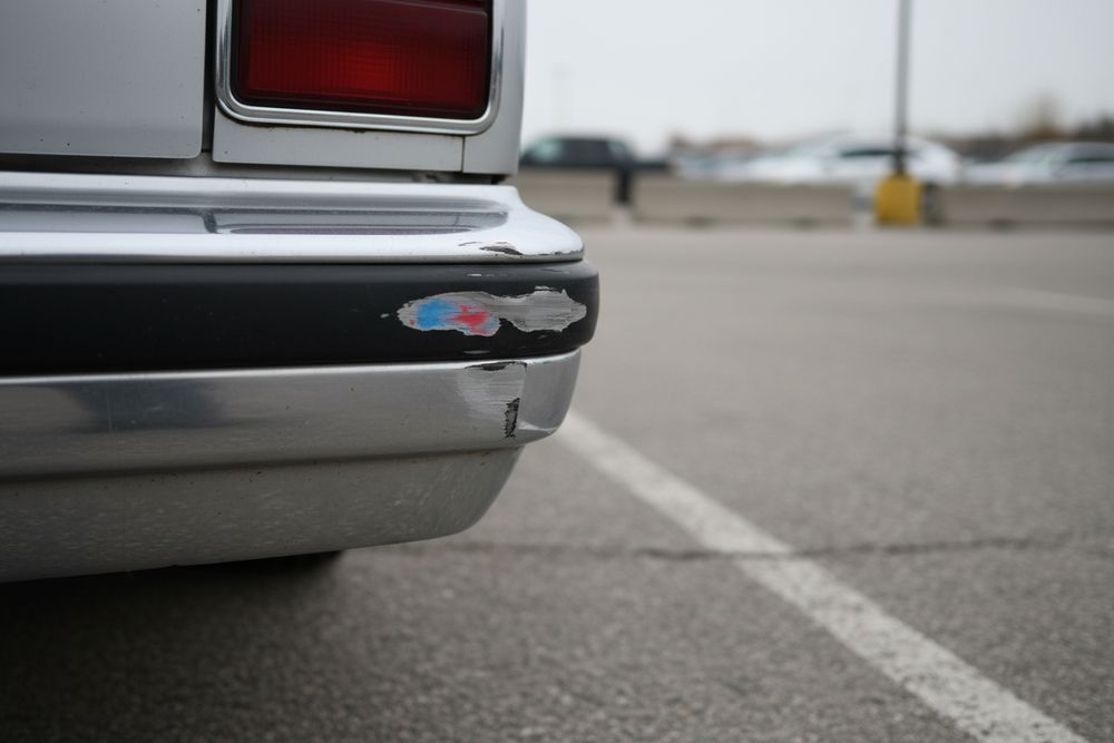 A scuffed and slightly dented rear bumper corner on an older silver car